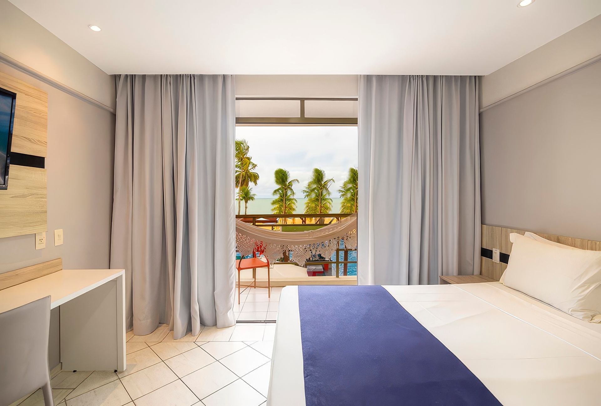 Um quarto de hotel com cama, escrivaninha, televisão e varanda. Netuanah Praia Hotel