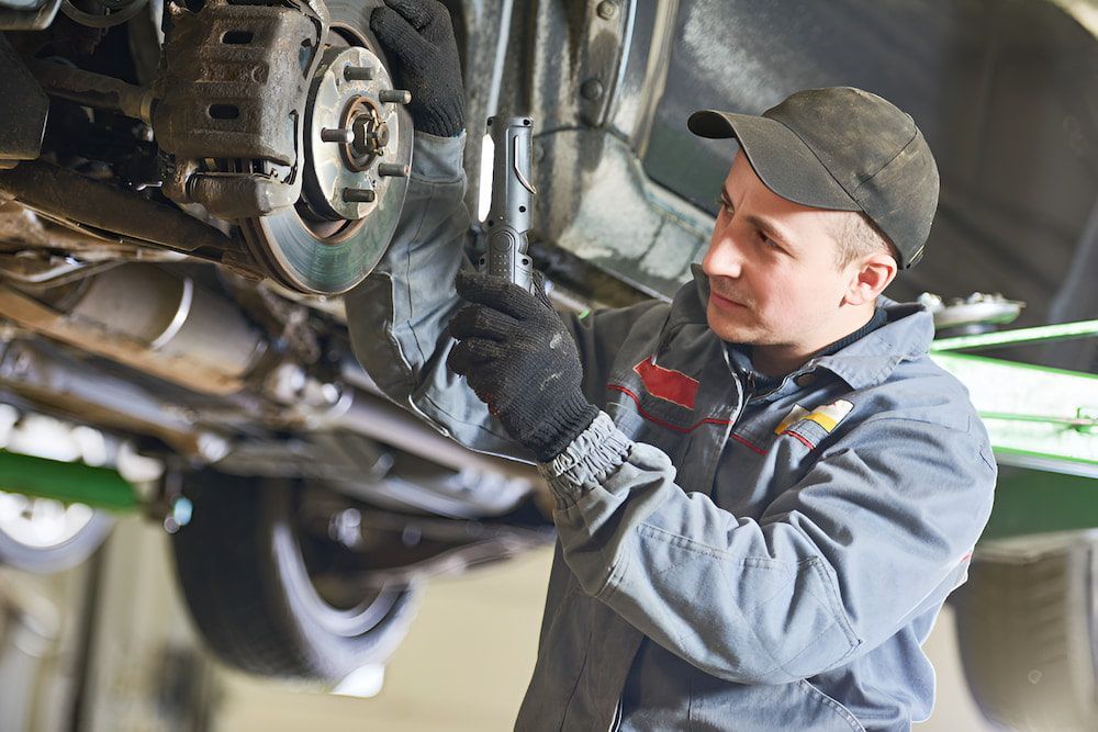 A Man Is Working On The Underside Of A Car In A Garage — Cameron Brothers Automotive In Currajong, QLD