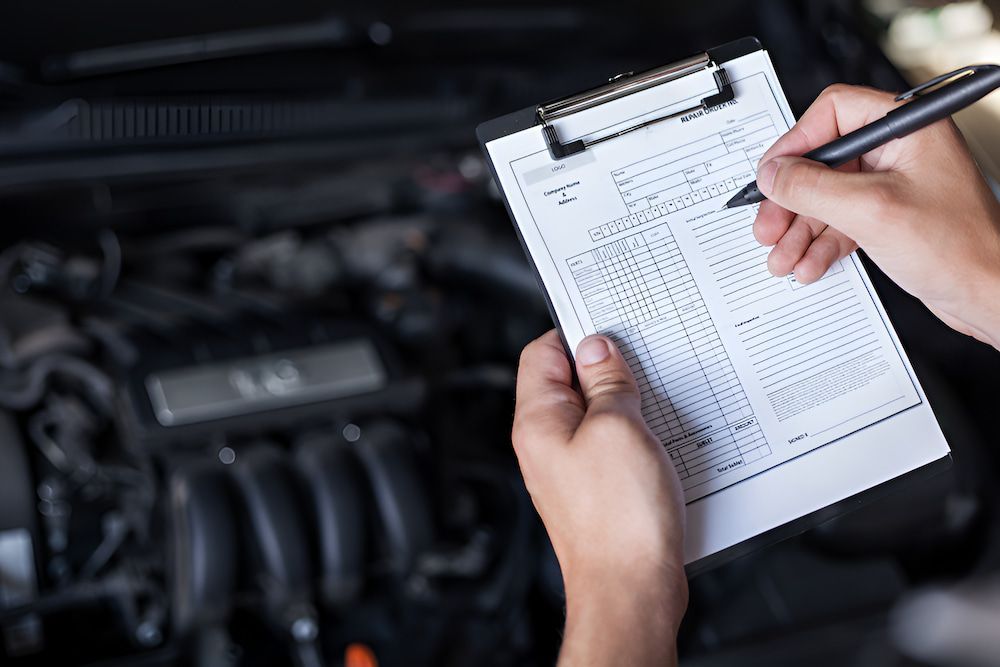 A Person Is Writing On A Clipboard In Front Of A Car Engine — Cameron Brothers Automotive In Currajong, QLD