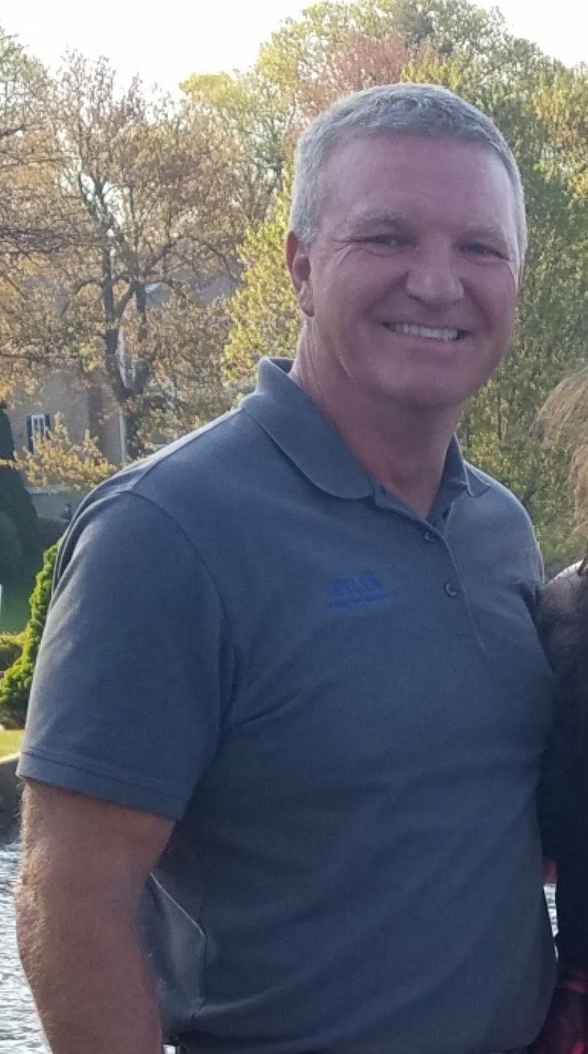 A man in a blue shirt and overalls with his arms crossed