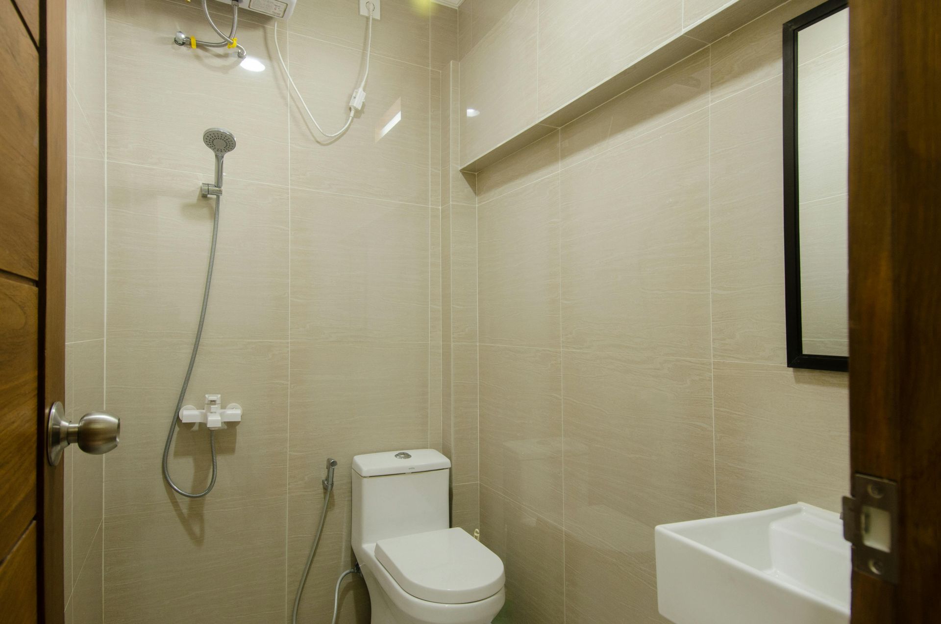 A modern, neutral-toned bathroom with a showerhead, a white toilet, and a wall-mounted sink below a mirror.