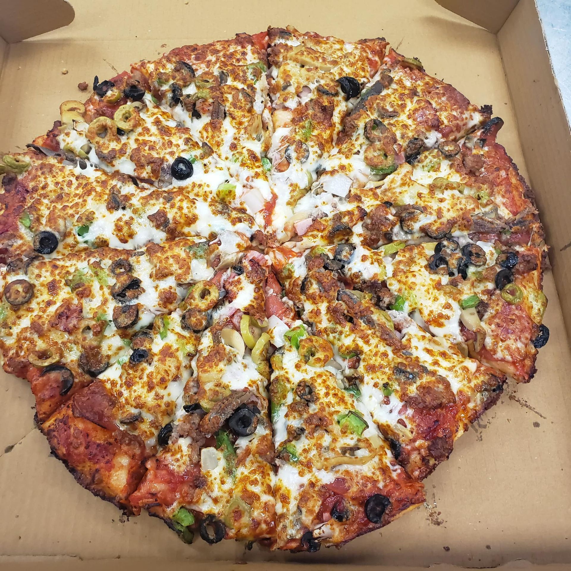 A pizza with a lot of toppings is in a cardboard box.