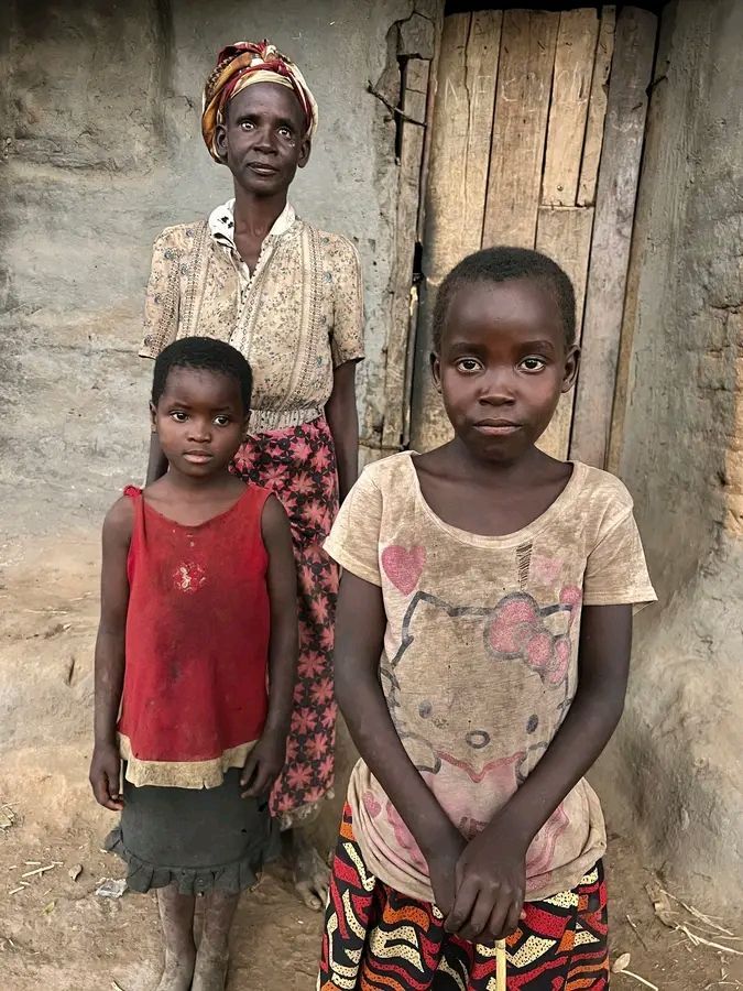 A woman and two girls stand in front of a weathered building; they look at the camera.