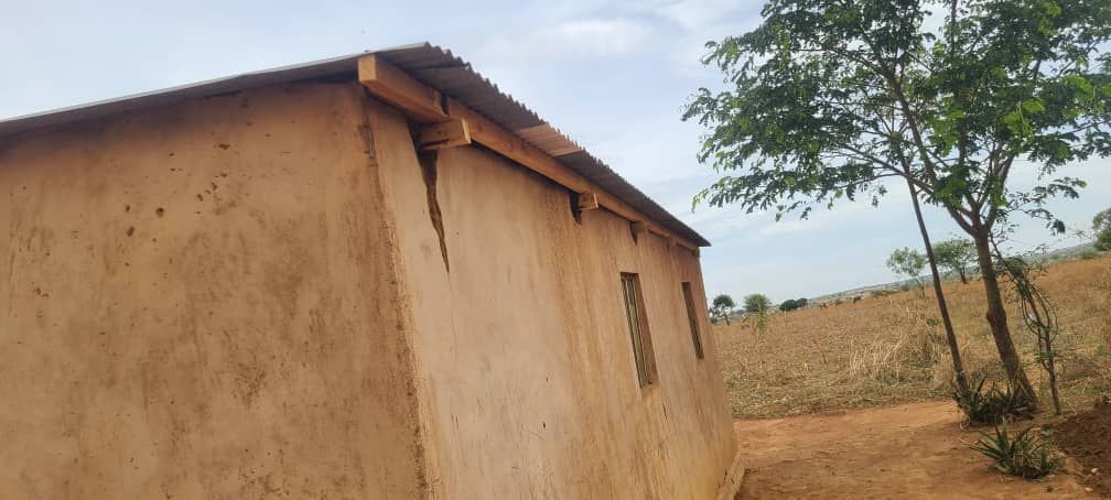A small house with a wooden roof is sitting in the middle of a field.