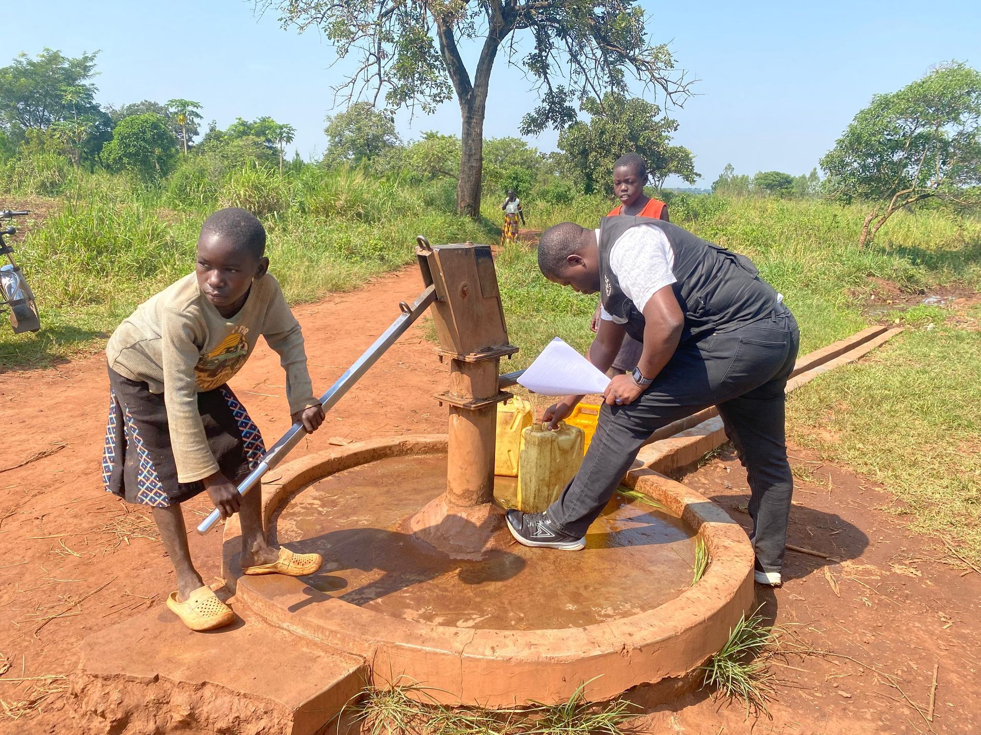 Nwoya, Uganda — the borehole in use with a child at the hand pump, June 2026.