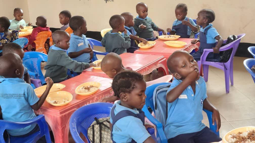Children in blue uniforms eating at tables in a brightly lit room.