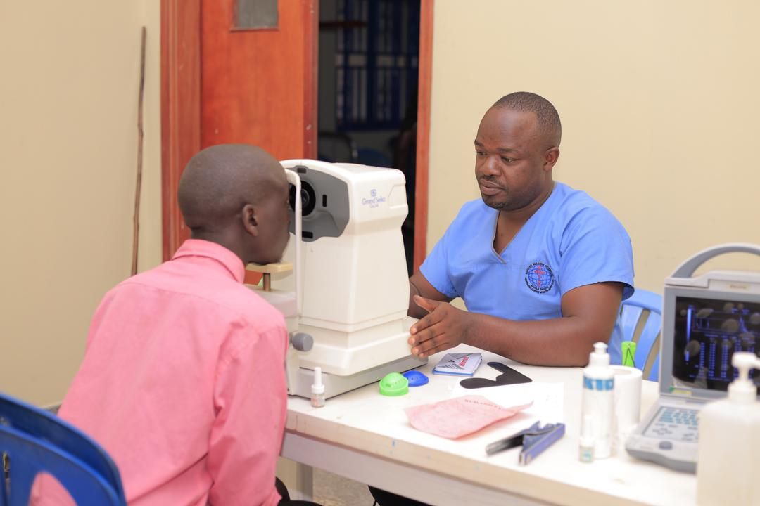 A man in a pink shirt is getting his eyes examined by an ophthalmologist.