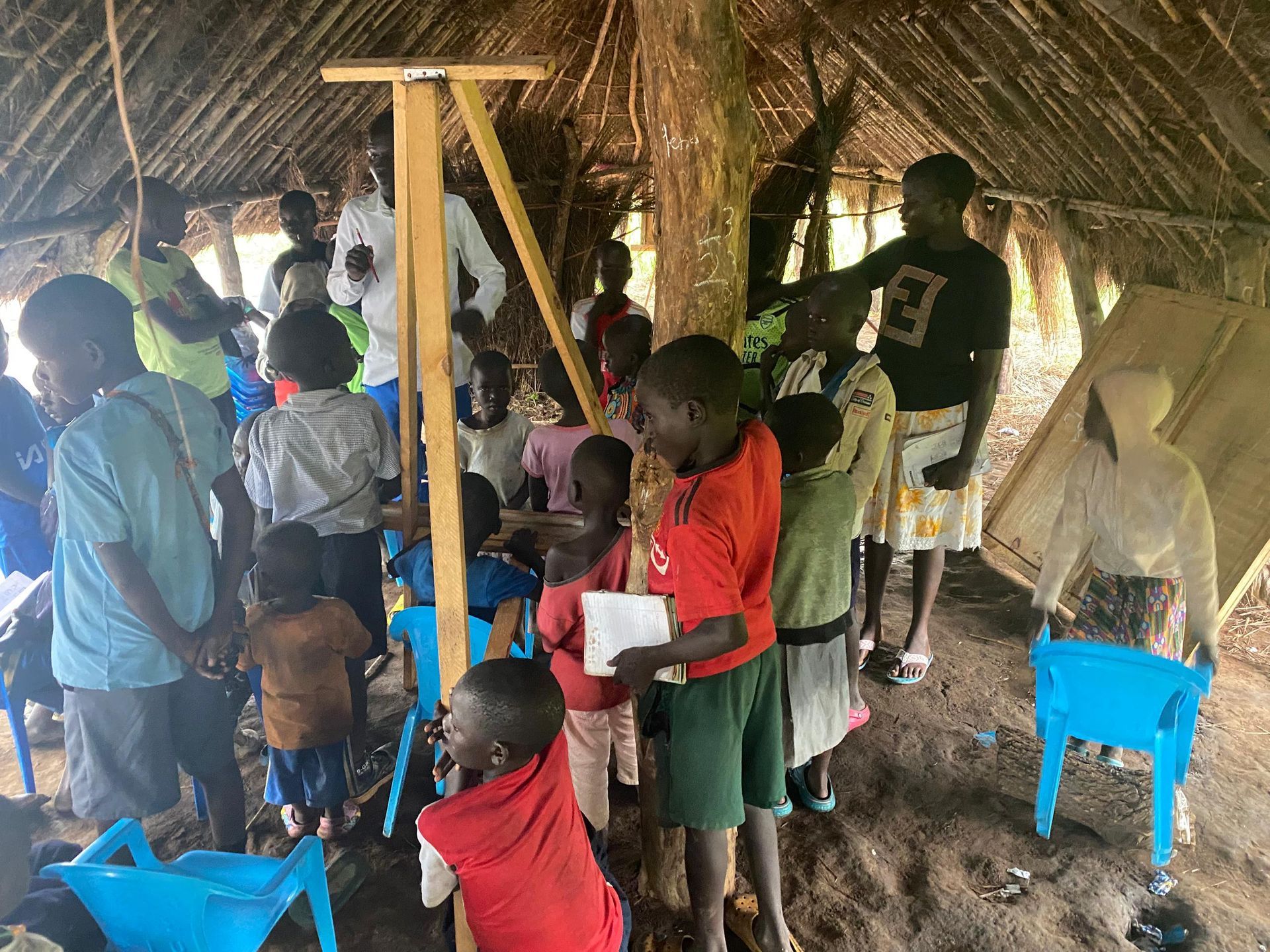 A group of children are standing in a hut under a thatched roof.