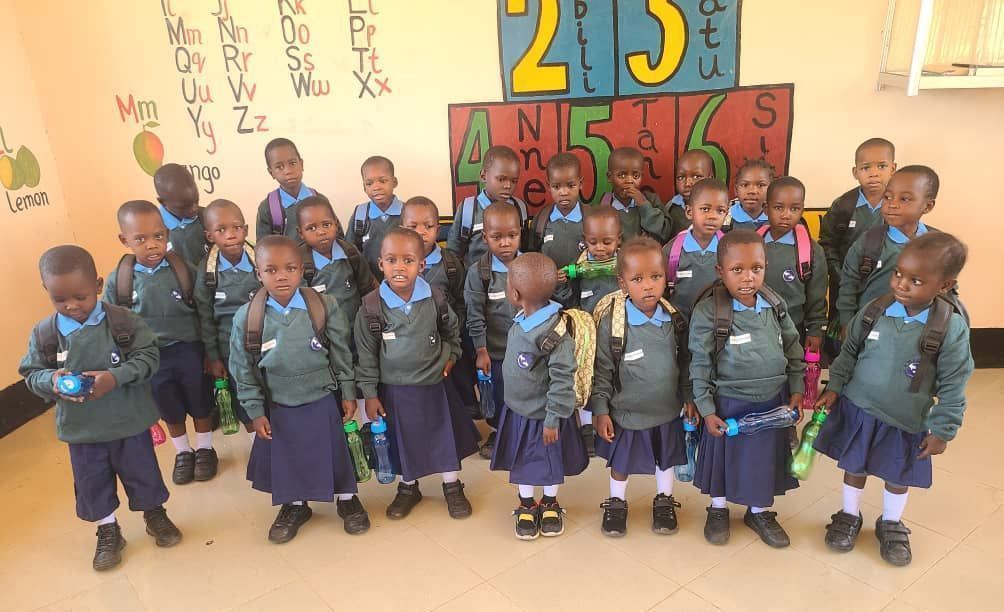 Children in school uniforms stand in a classroom with backpacks and water bottles.