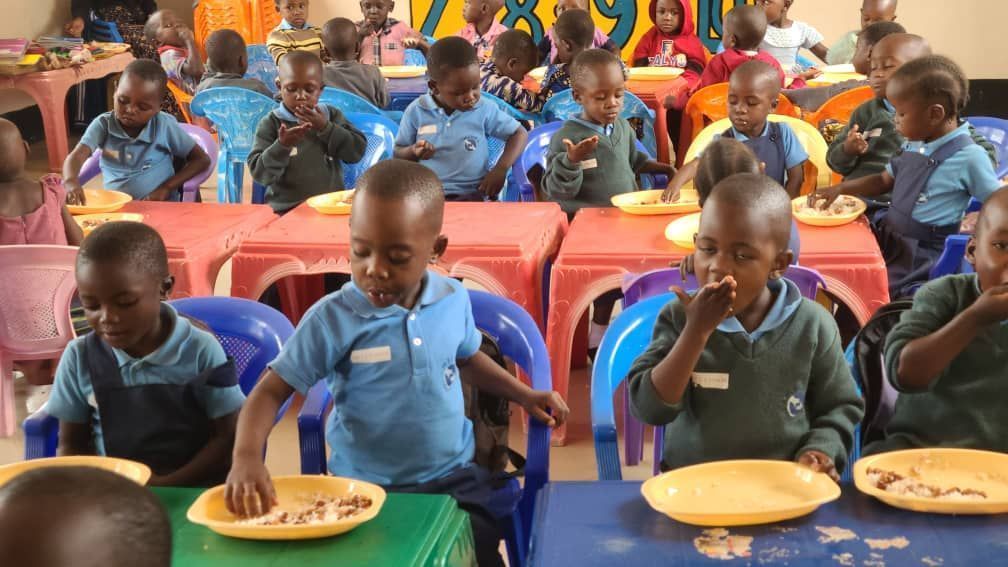 Children eating food at tables in a classroom.