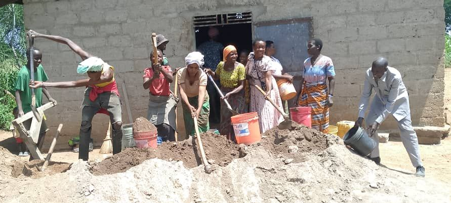 Group of people working outdoors, shoveling and mixing materials. Building site with a concrete block building.