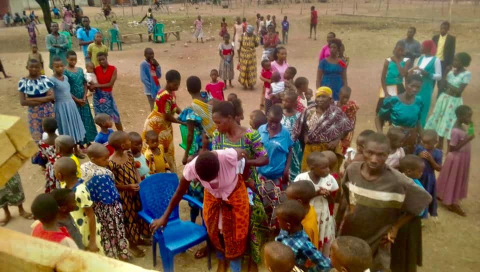 A large group of people are standing in a dirt field.