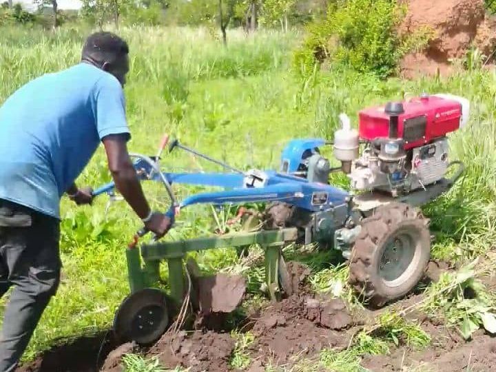 a man is plowing a field with a small tractor, thanks to the efforts of Amigos Internacionales and it's Demonstration Farms