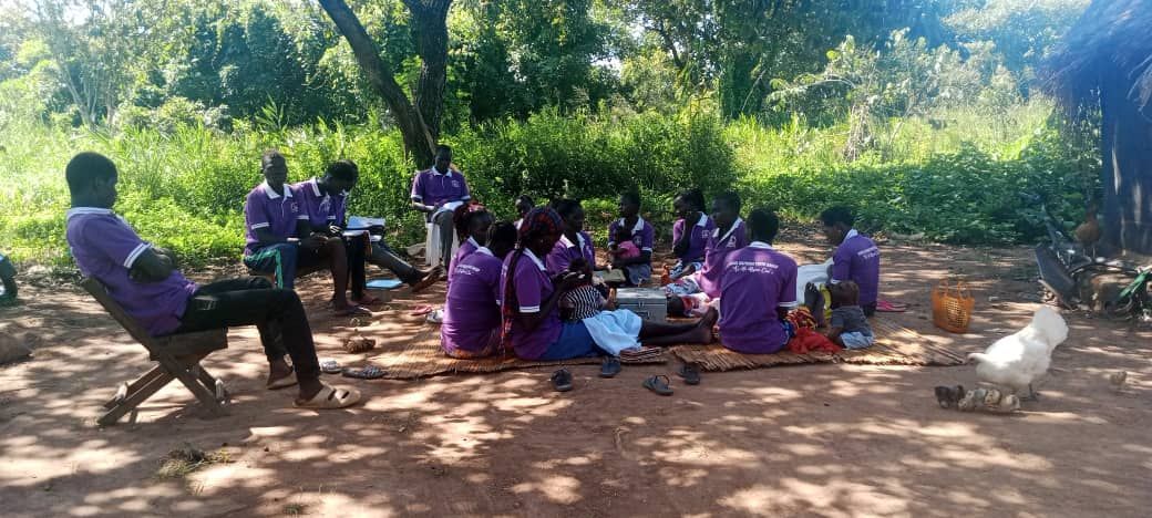 A group of people are sitting around a table in the woods.