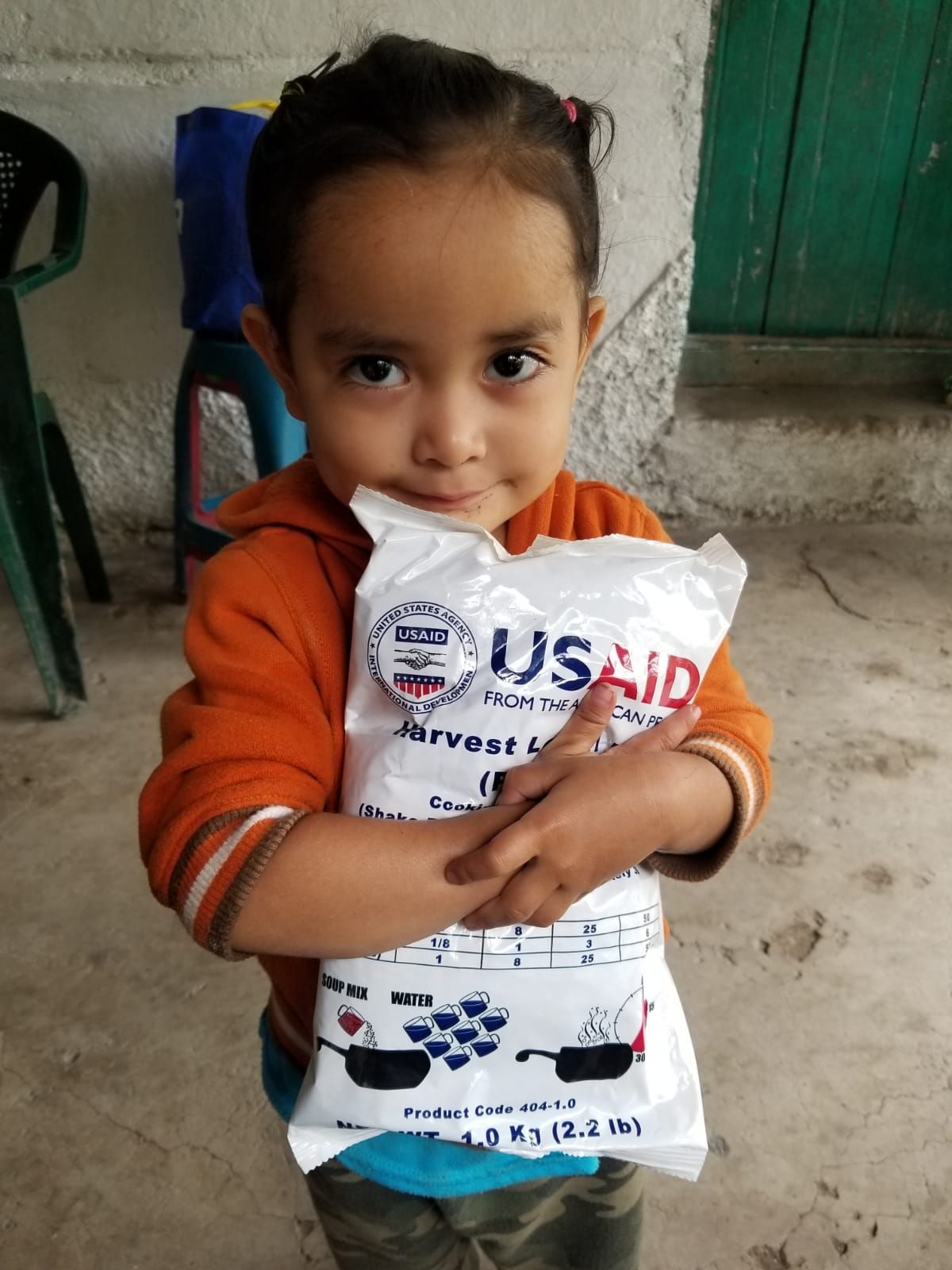 Child holding USAID food packet connected to Amigos Internacionales food distribution work