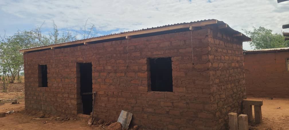 A small brick building with a wooden roof is being built in the middle of a field.