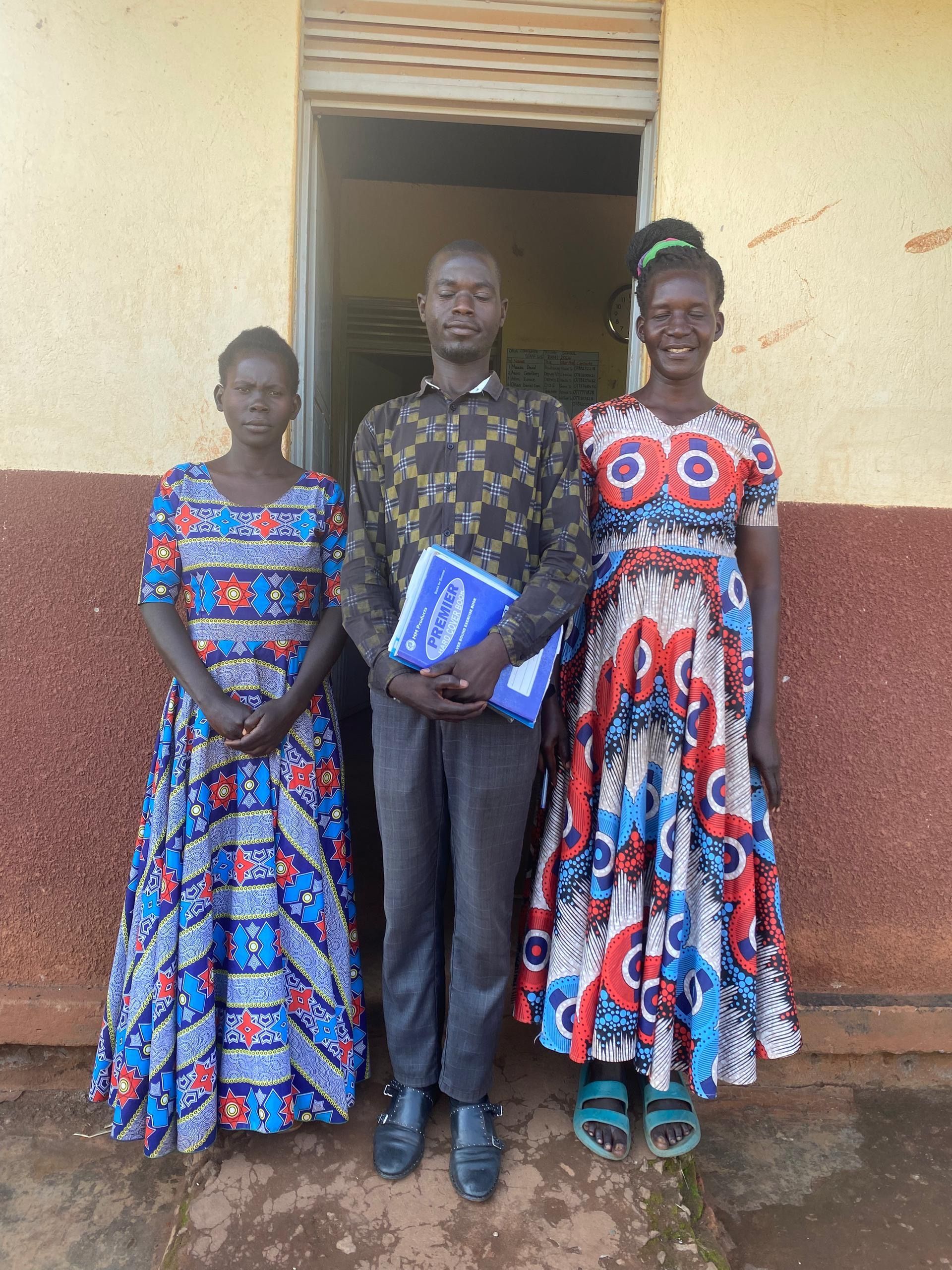 Nwoya, Uganda — two women from the community in patterned Ugandan dresses on the school grounds, June 2026.
