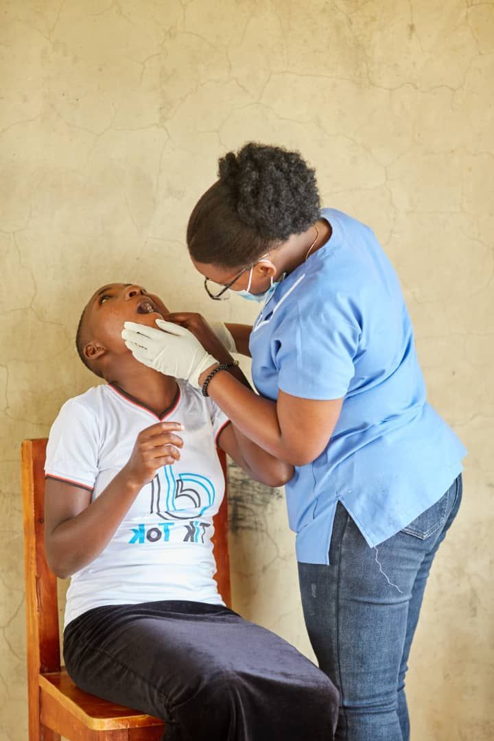 A woman in a white shirt with the number 15 on it is being examined by a nurse at Medical Camp in Ogul Village.