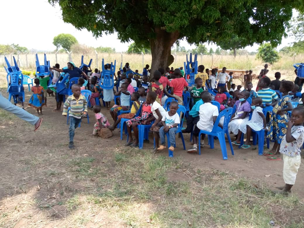 A group of people are sitting in blue chairs under a tree.