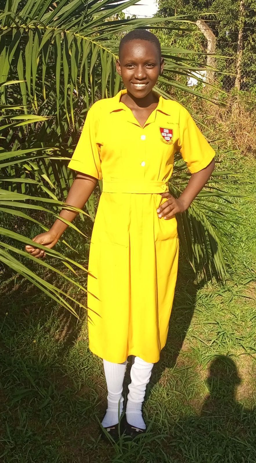 Young person in yellow school uniform standing outdoors, smiling.