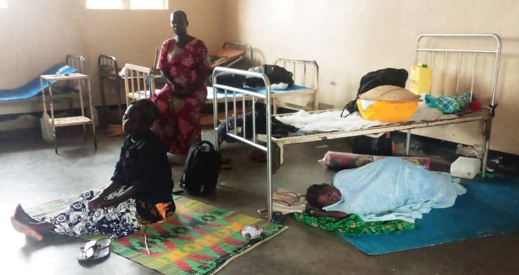 A woman is standing next to a woman laying on the floor in a hospital room.