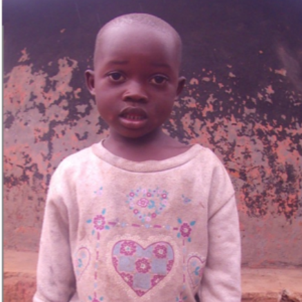 Young child wearing a patterned light-colored shirt, standing in front of a mottled wall.