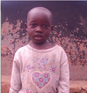 Child standing, wearing a light-colored sweater with a heart design and a denim skirt; bare feet.