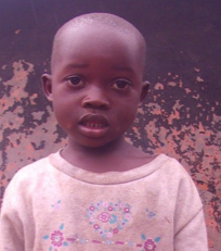 Child wearing a light-colored sweater with a heart design stands in front of a weathered wall.