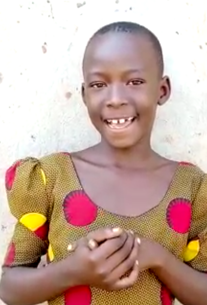 Young person with shaved head, smiling, wearing a patterned dress with red, yellow, and brown colors.
