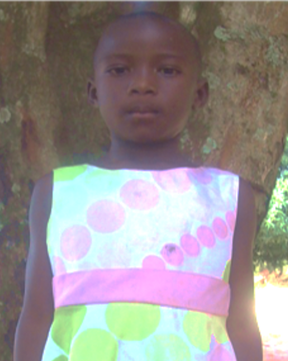 Young girl stands in front of a tree, wearing a polka-dot dress with pink and green circles, and a pink waistband.