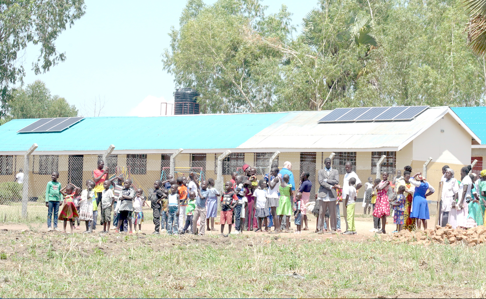 A group of people are standing in front of a building with solar panels on the roof.