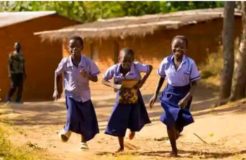 Three students in school uniforms running outside a rural school.