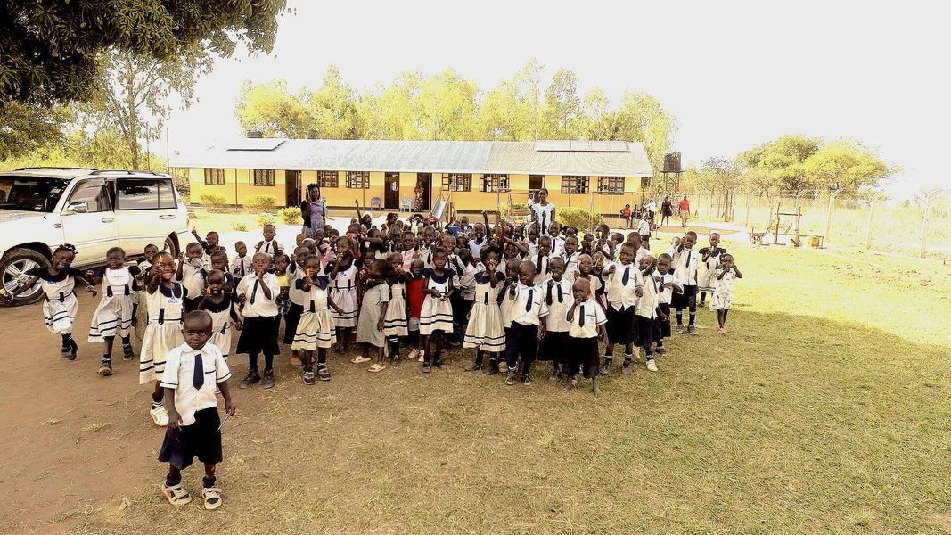 Schoolchildren in uniforms gathered outdoors near a yellow building.