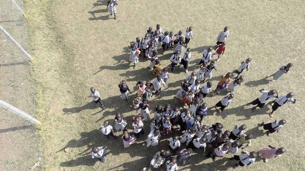 A large group of people on a dry, grassy field; long shadows indicate it's daytime.
