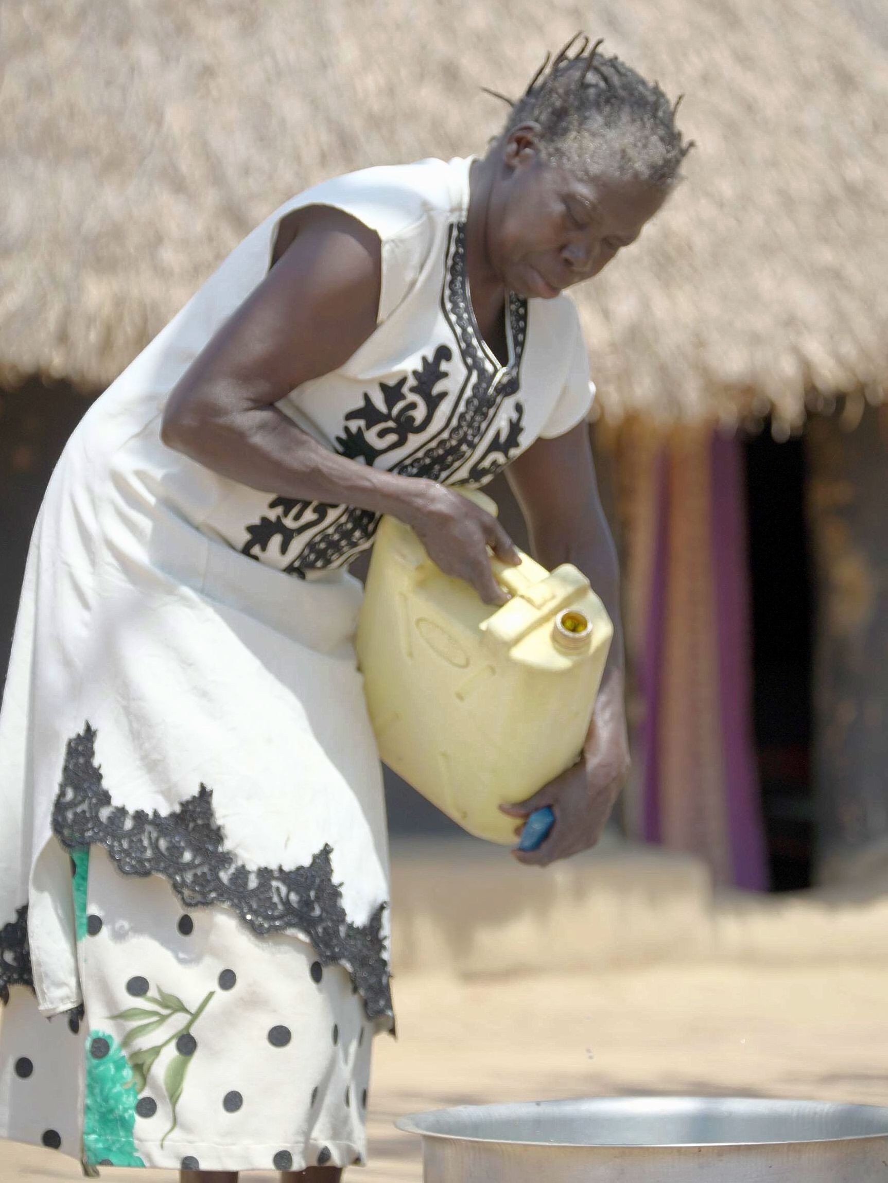 a woman in a white dress is pouring water into a pot .
