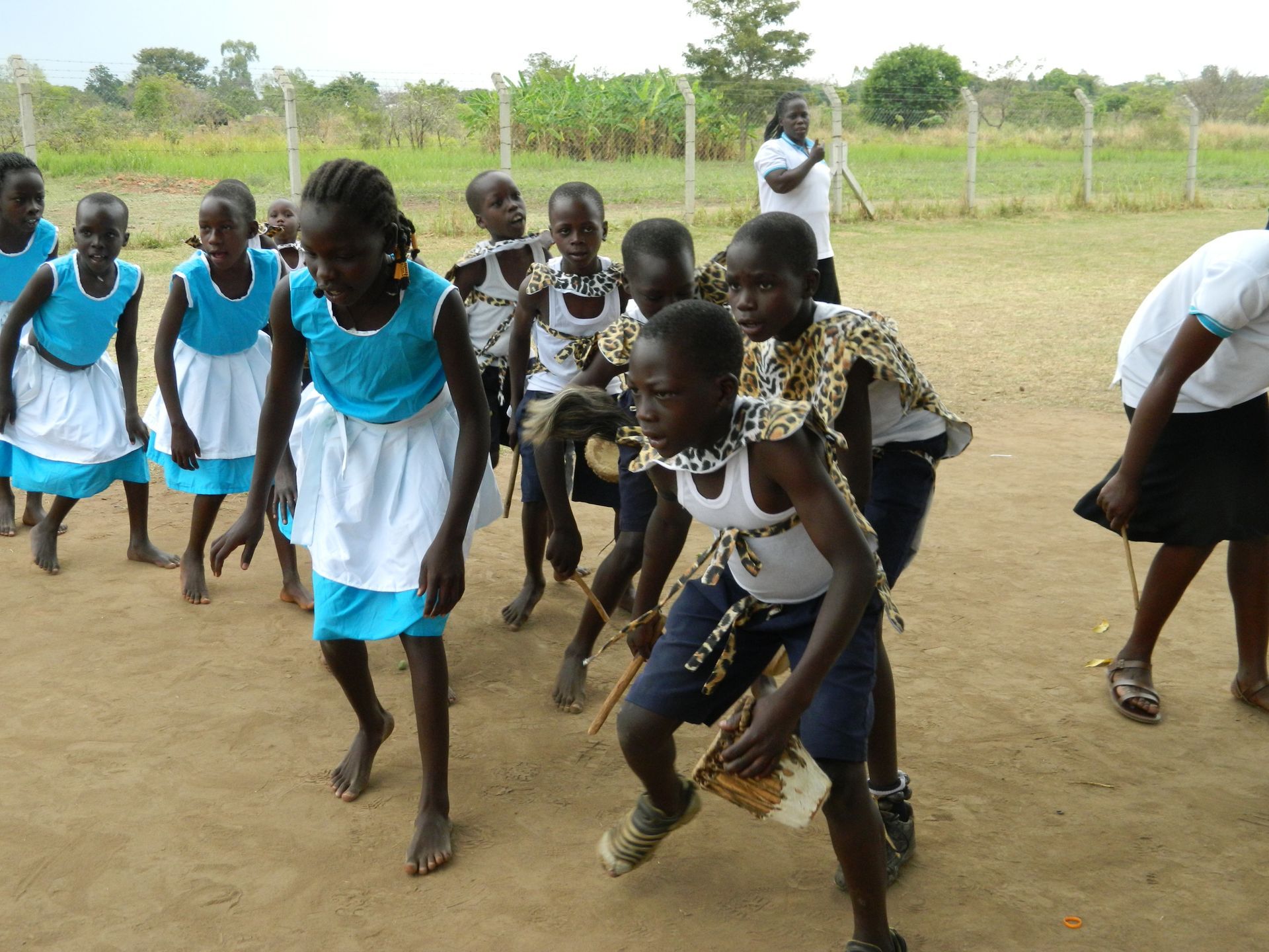 A group of children are dancing in a dirt field