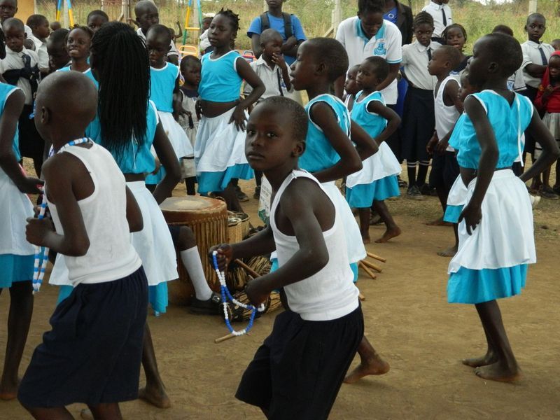 Children dancing outdoors in blue and white outfits, drums in the background.
