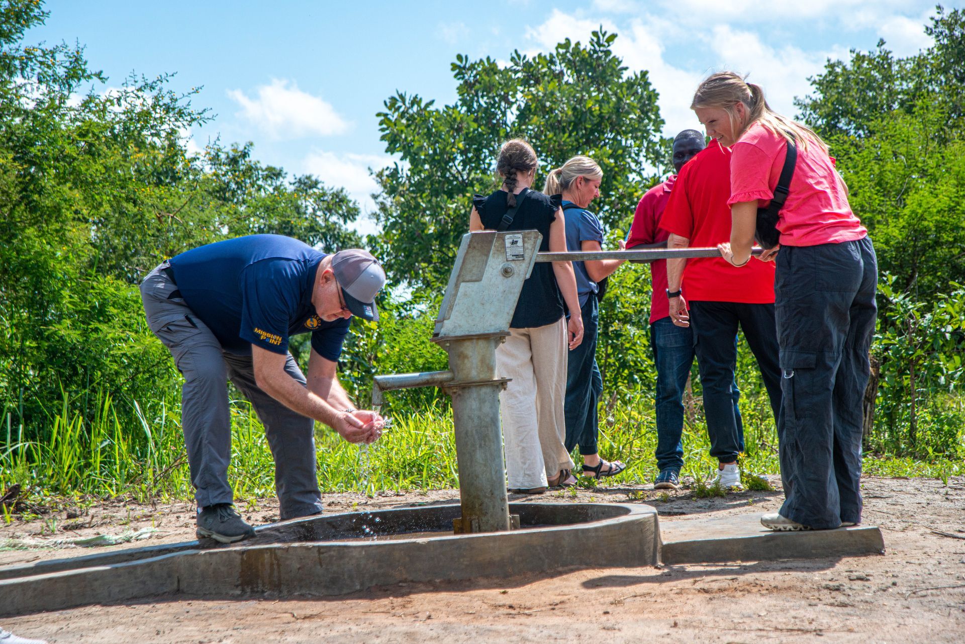 A group of people are standing around a water pump.