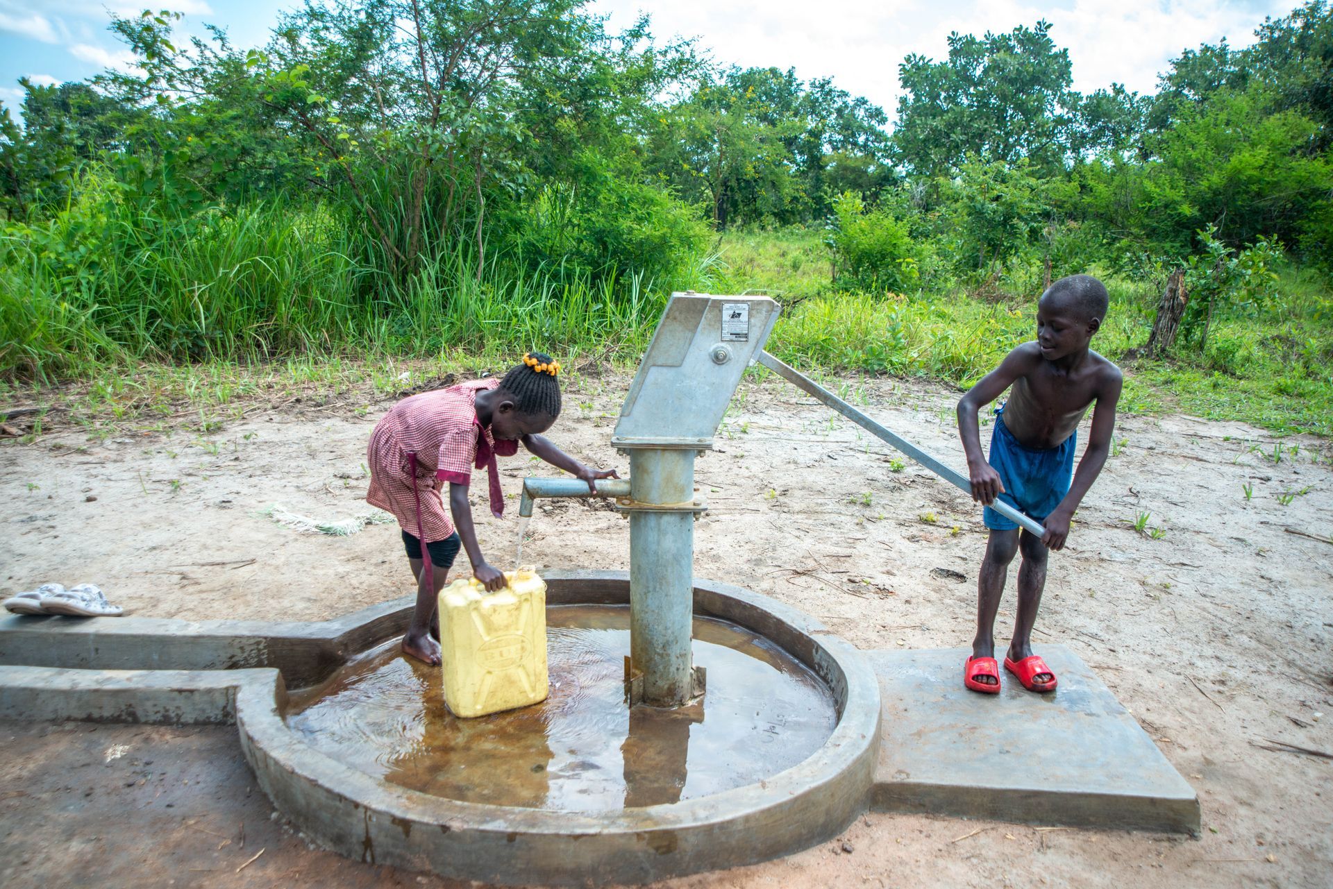 A boy and a girl are pumping water from a well.