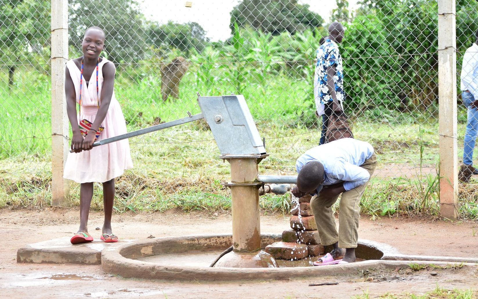 A group of people are standing around a water pump.