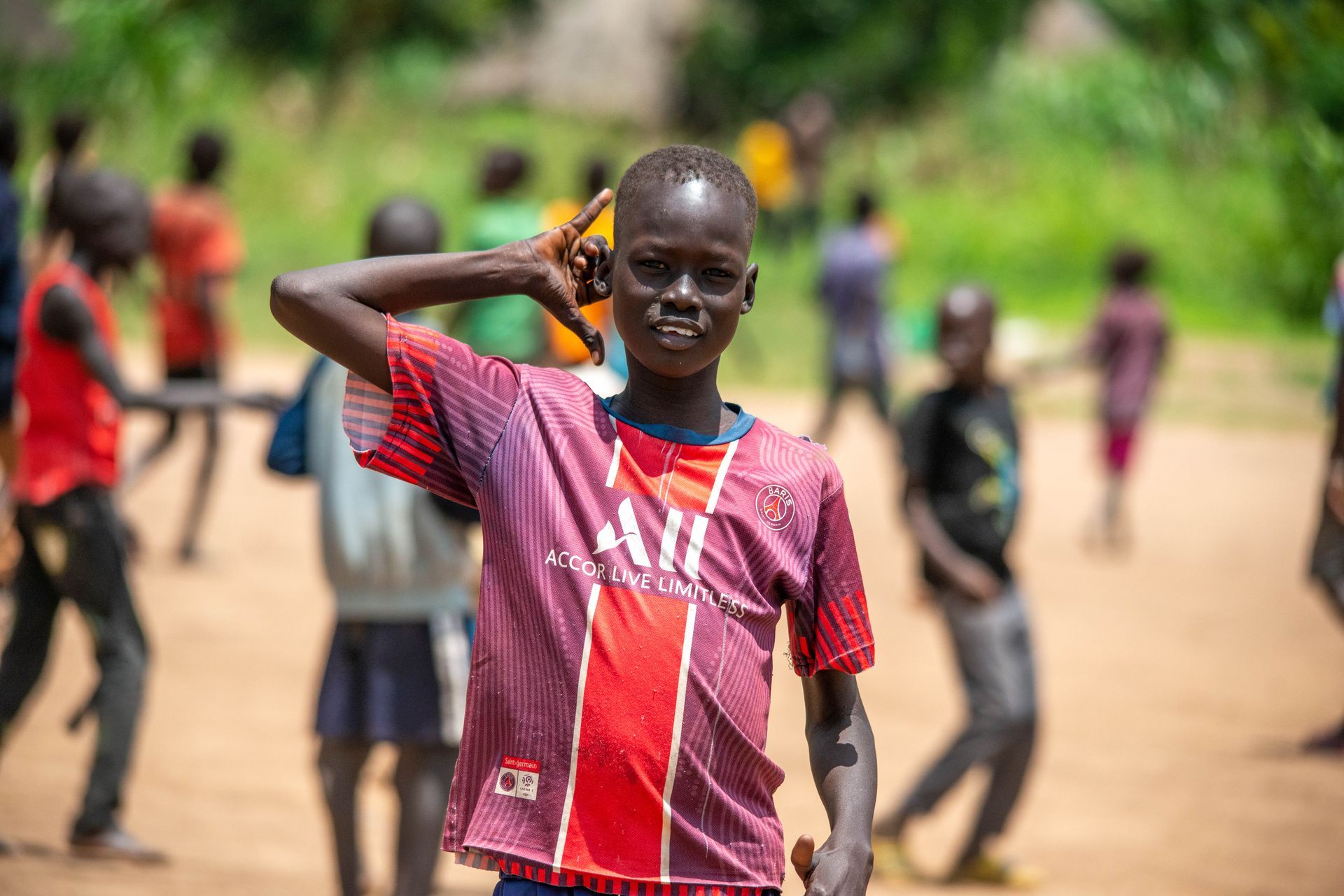 A young boy in a red and purple shirt is standing in front of a group of children.