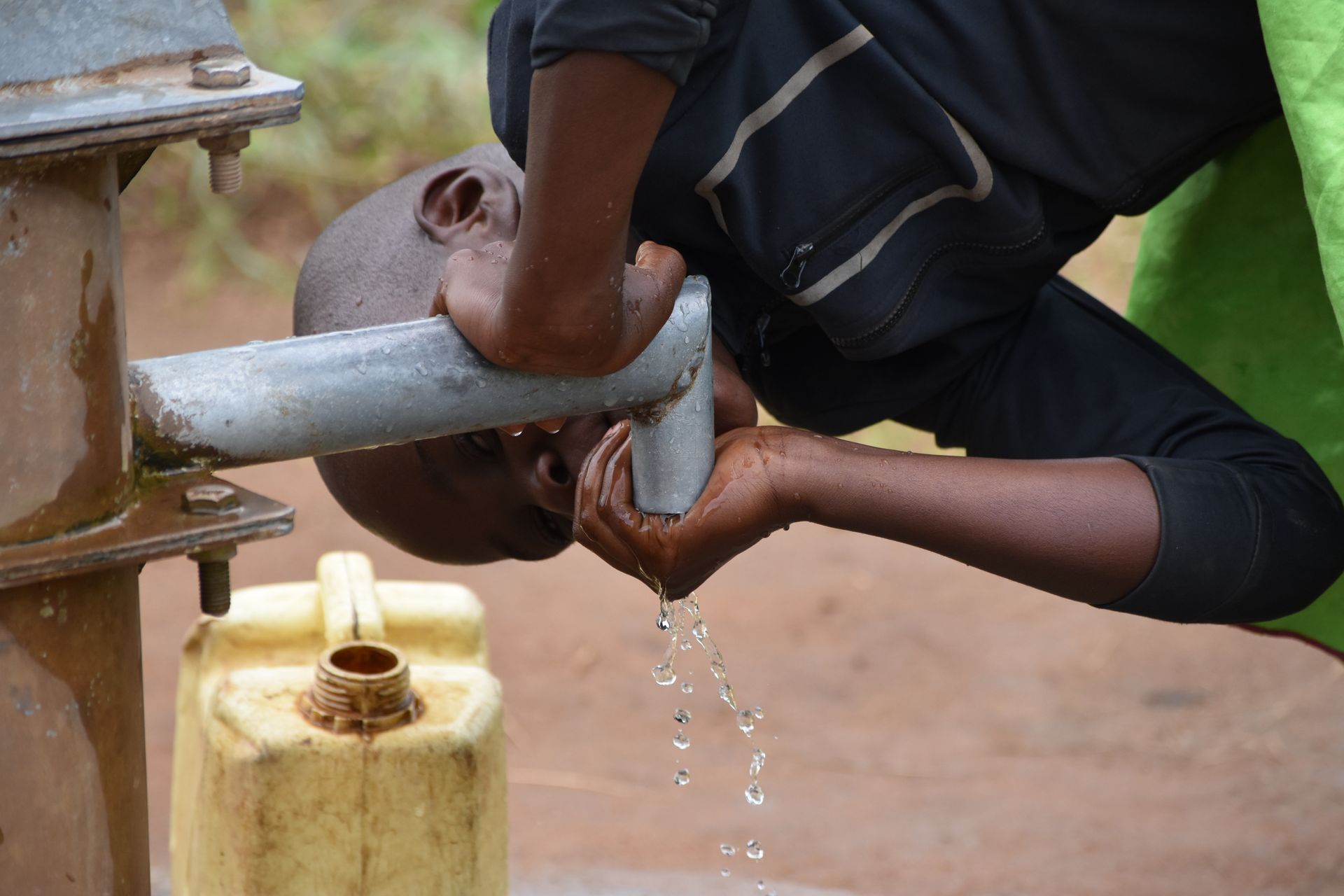 A man is drinking water from a water pump.
