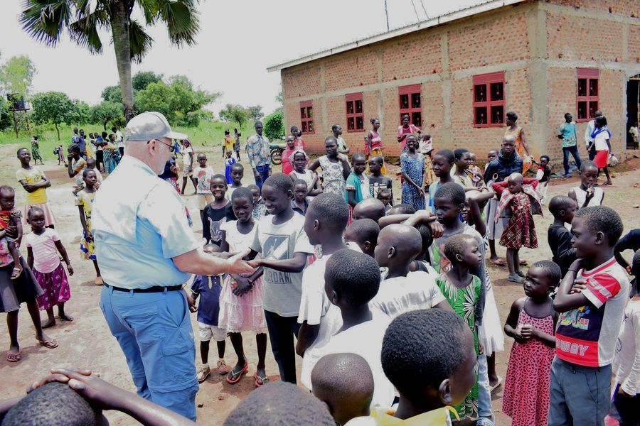 Man hands out items to a group of children outside a brick building.