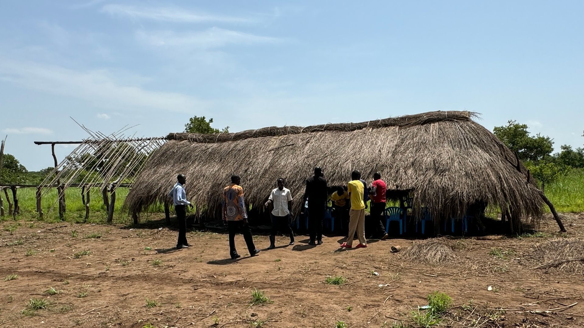 A group of people are standing in front of a thatched hut.