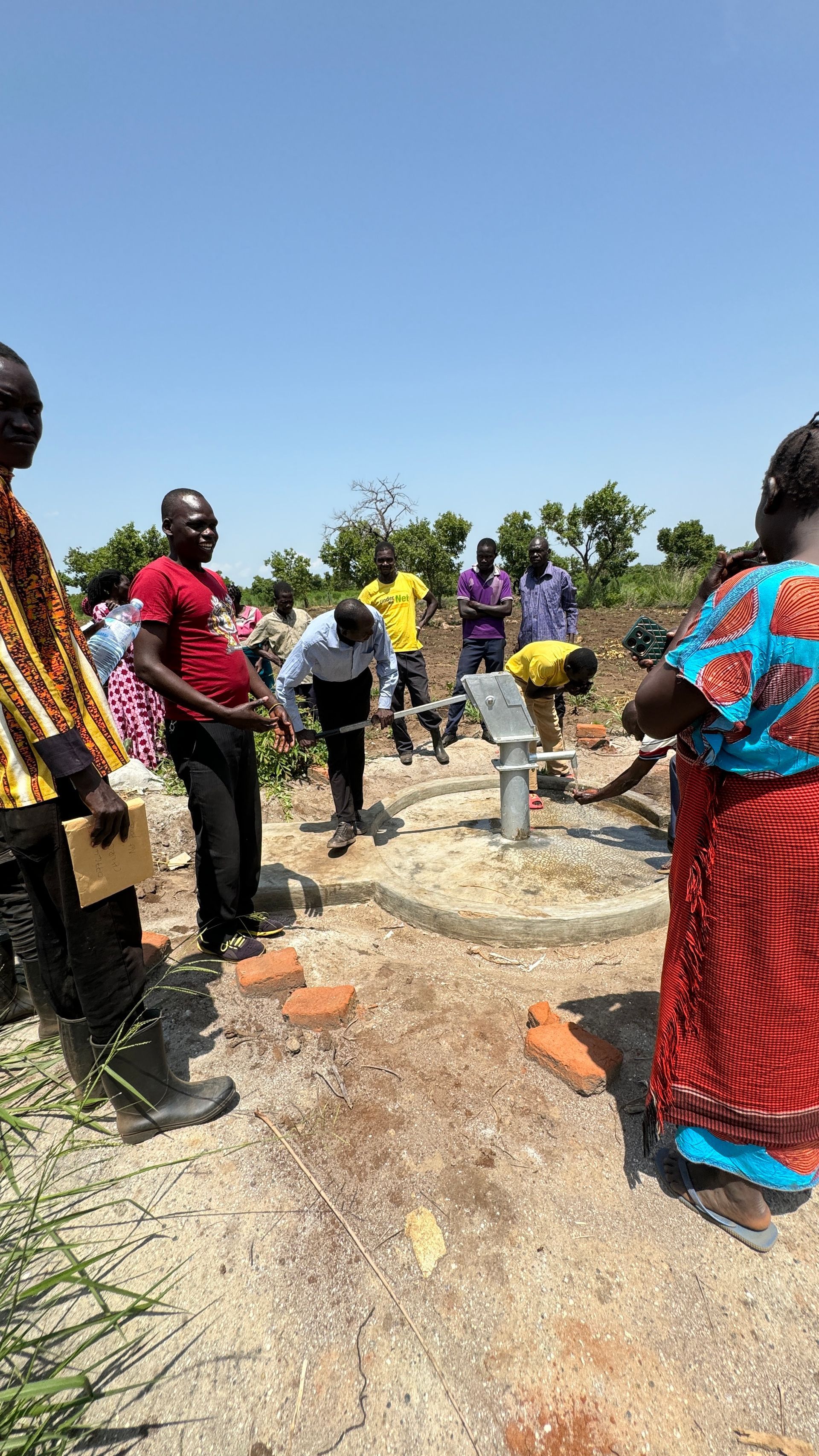 A group of people are standing around a water pump.