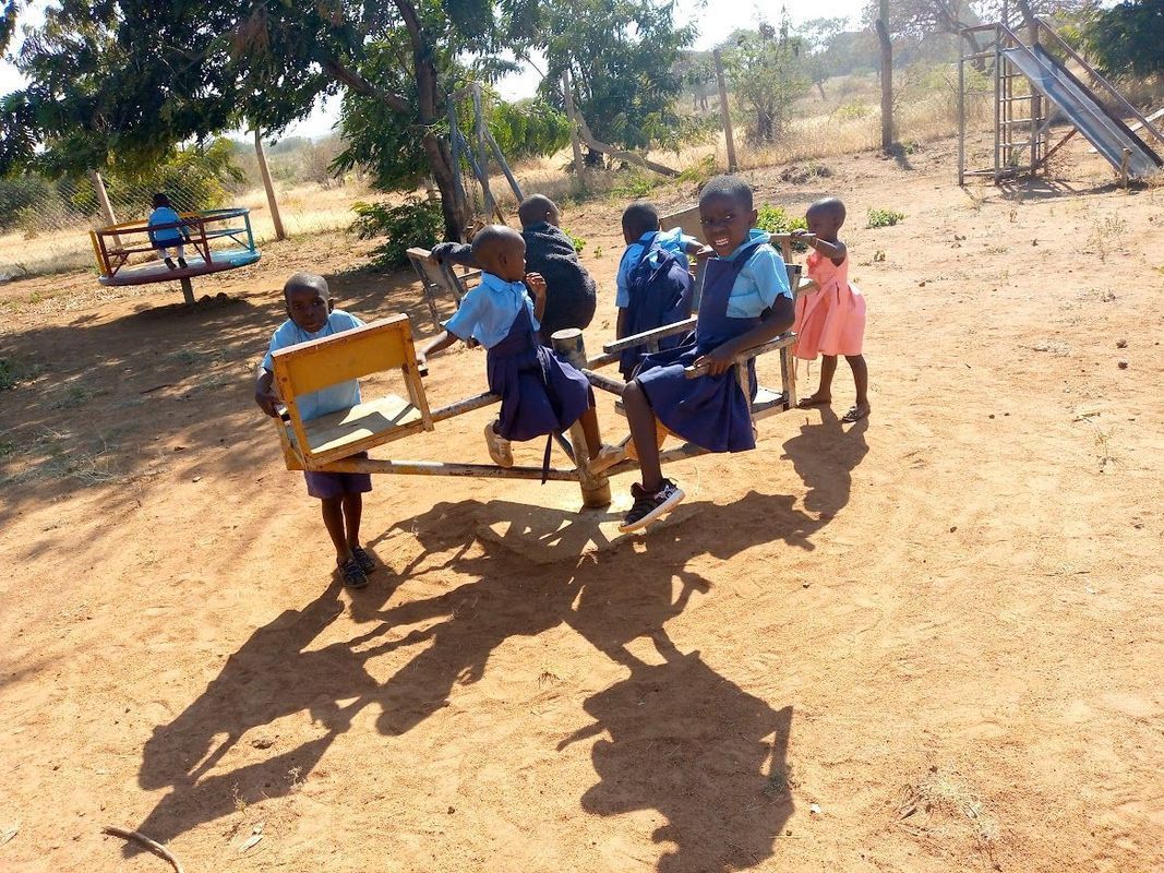Children playing on a handmade seesaw in a dry, outdoor setting.
