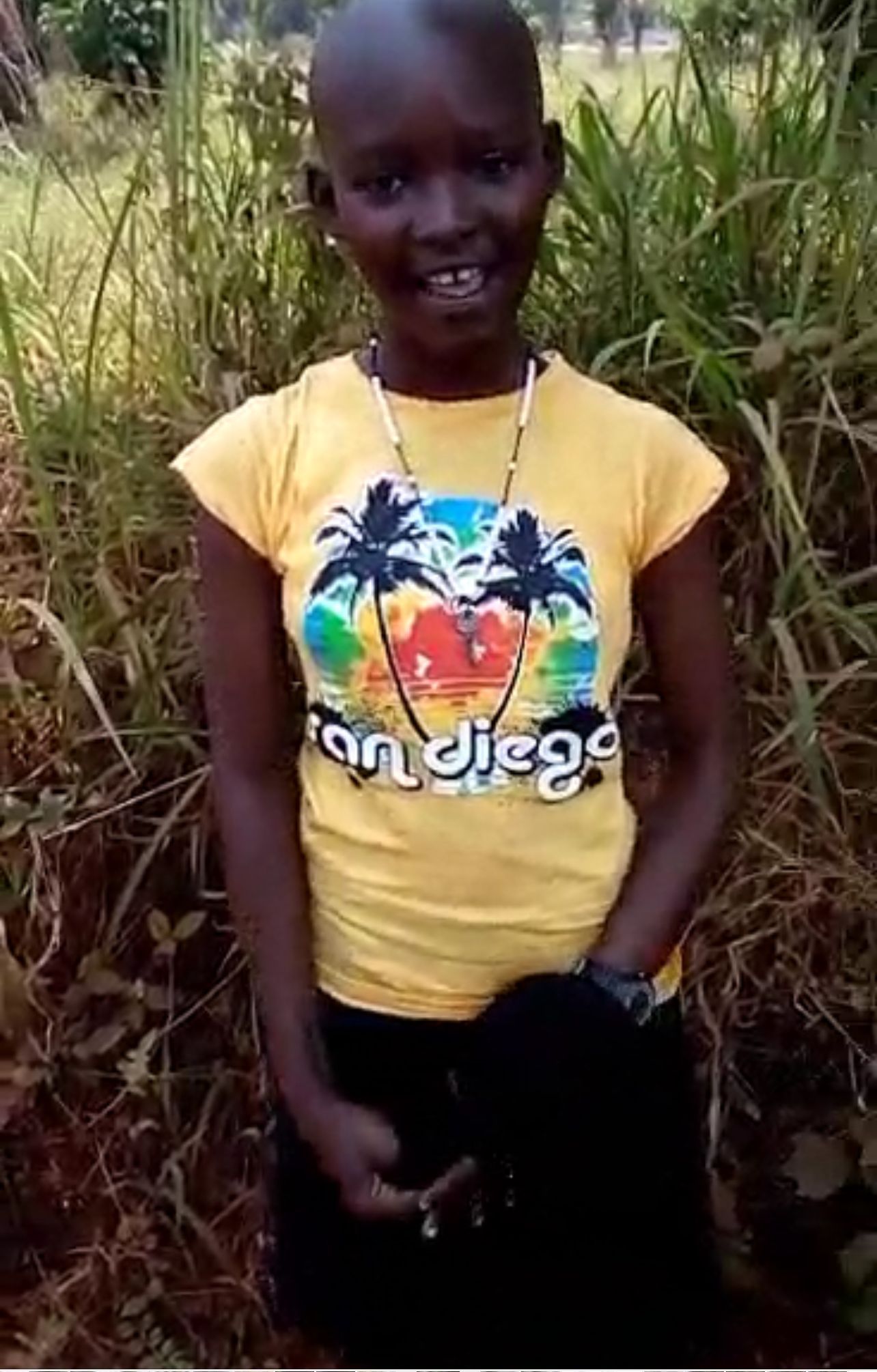 Young person wearing a yellow San Diego t-shirt, standing outdoors in front of tall grass.