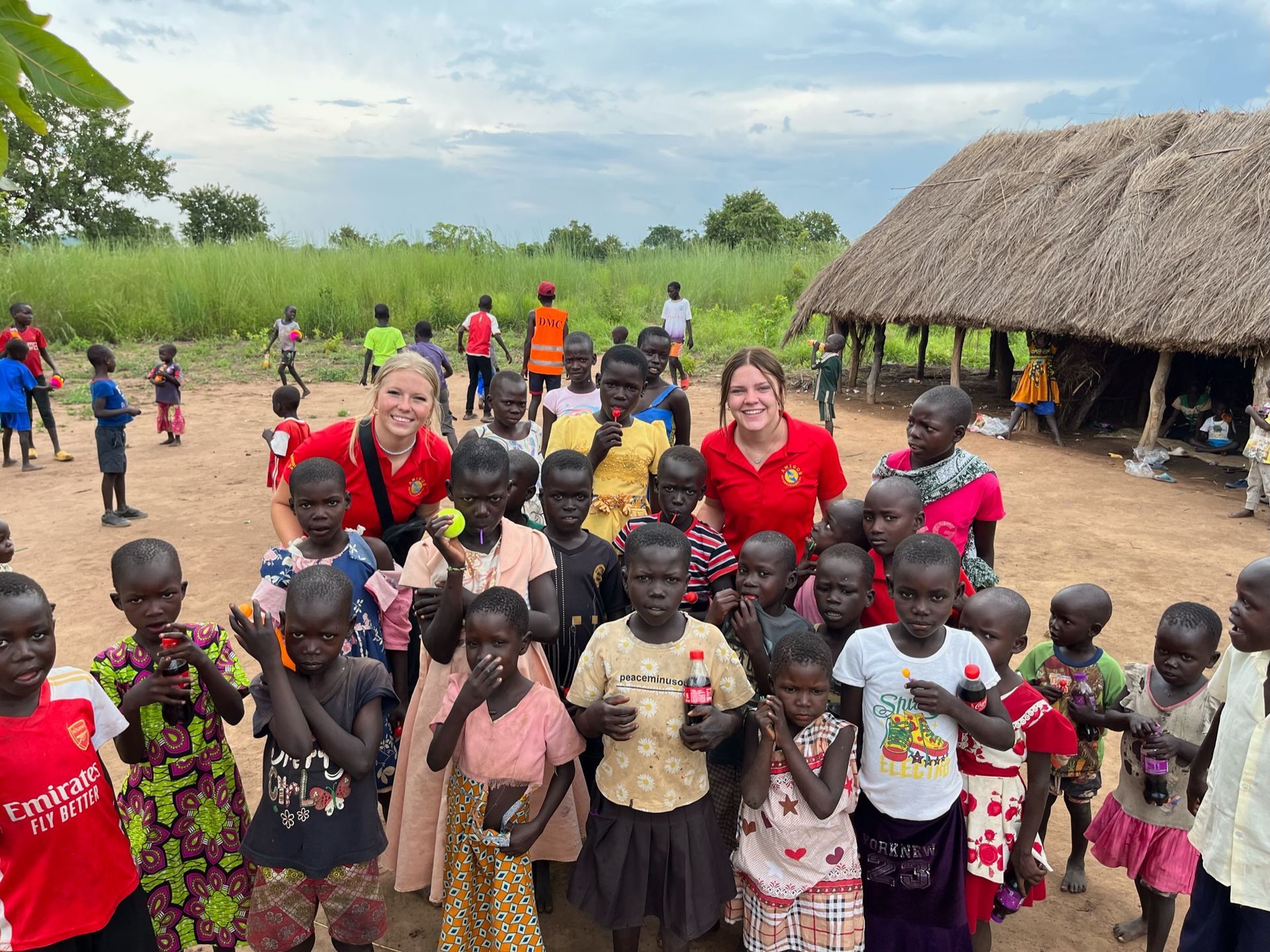 A group of children are posing for a picture in front of a thatched hut.