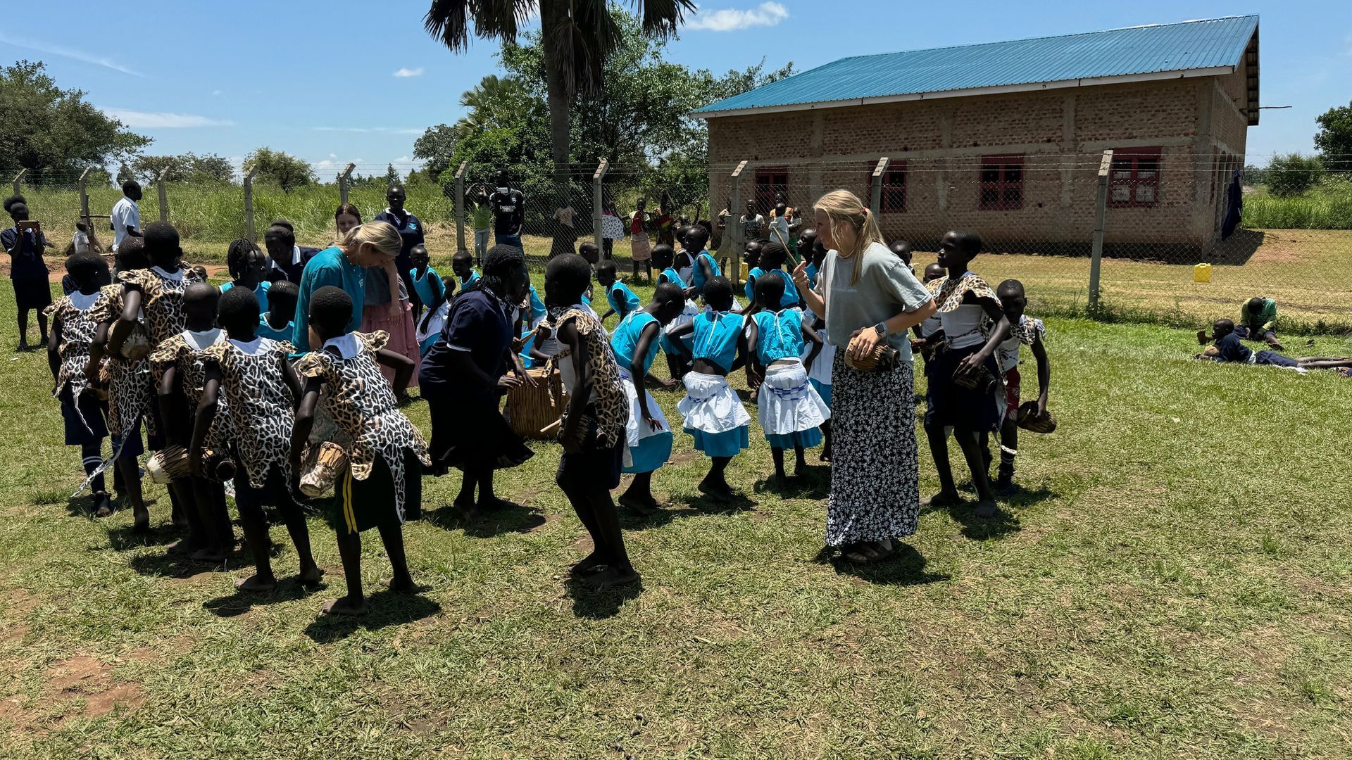 A woman is standing in front of a group of children in a field.