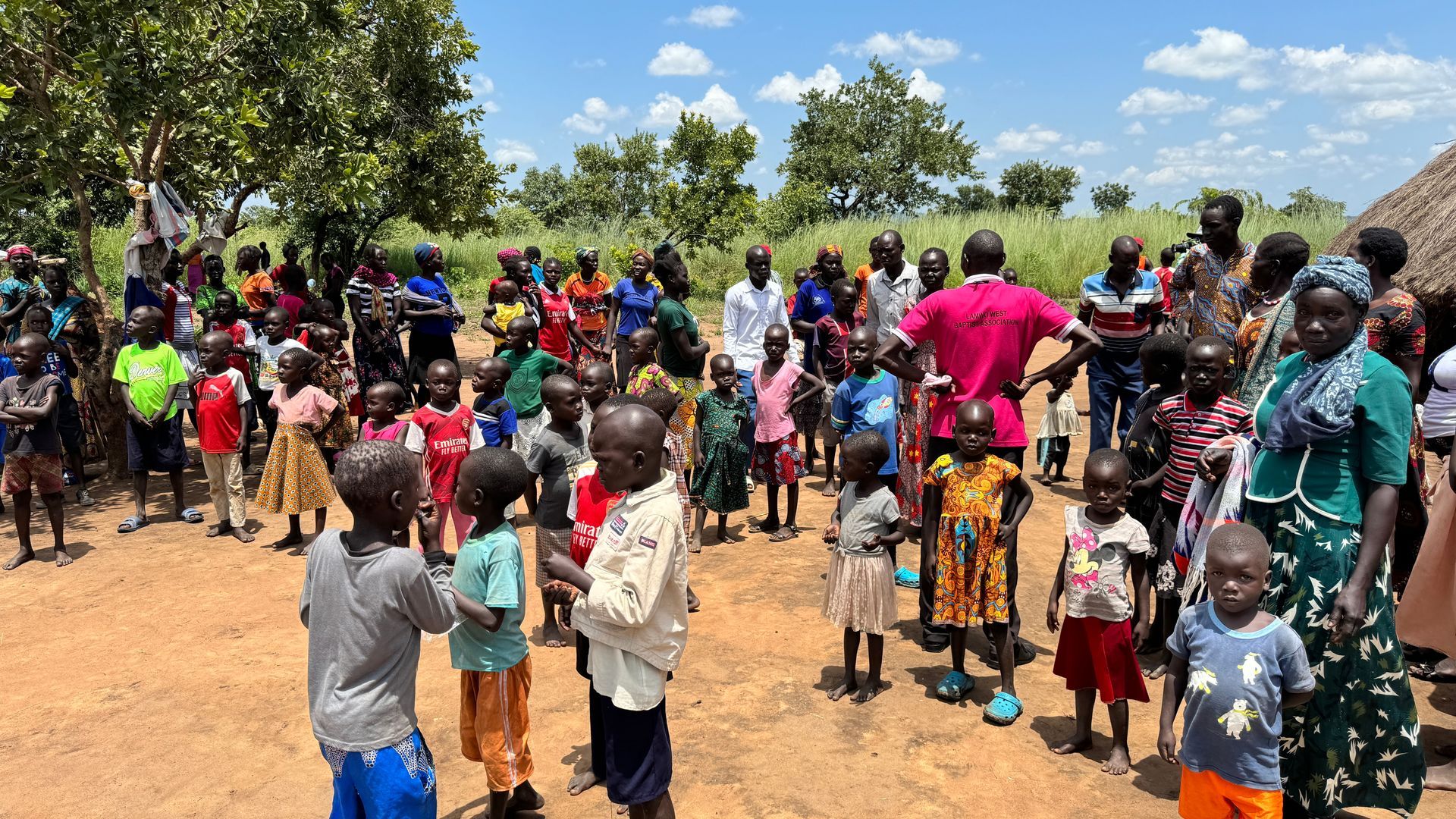 A large group of people are standing in a dirt field.